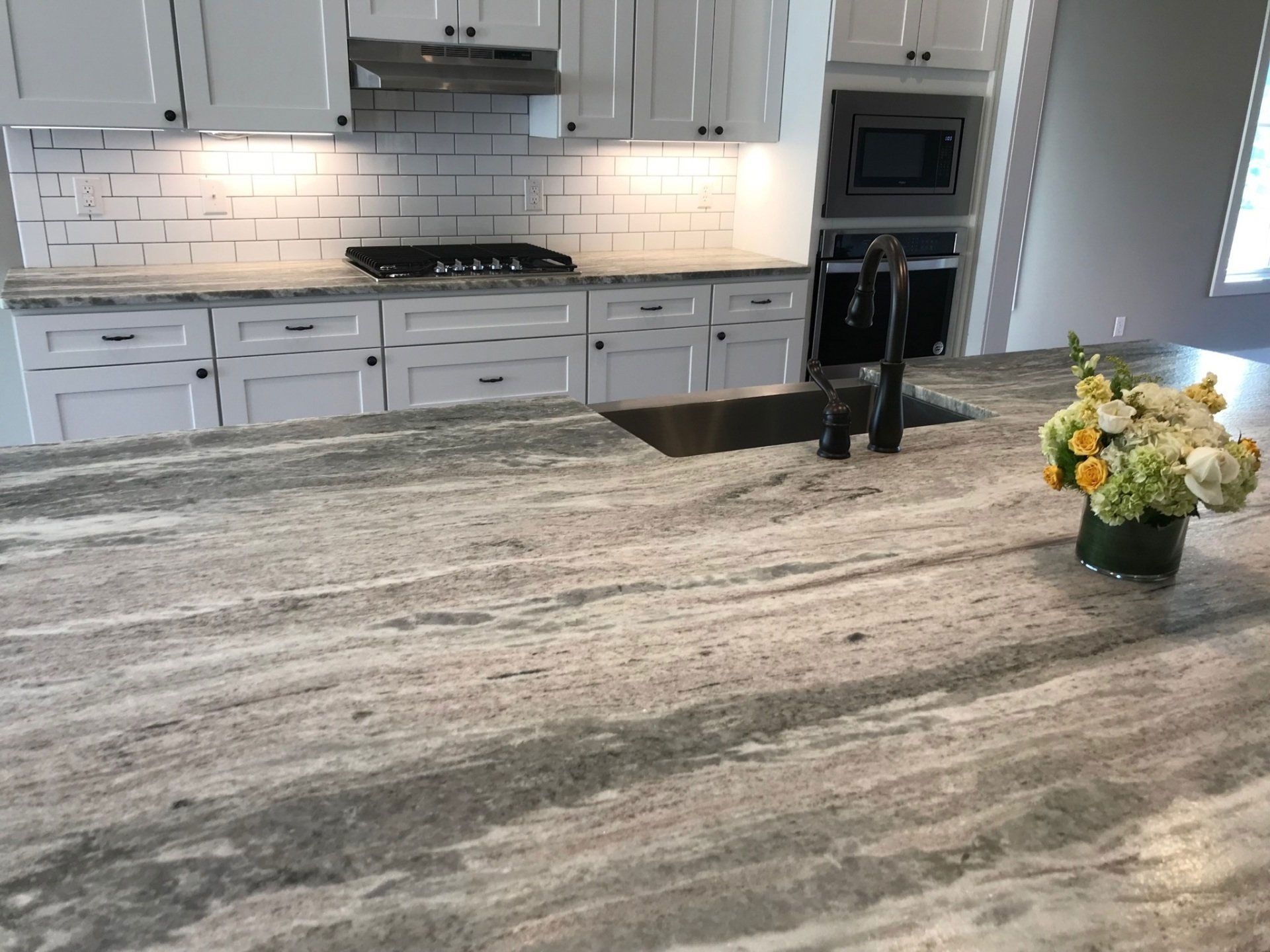 There is a vase of flowers on the counter in the kitchen.