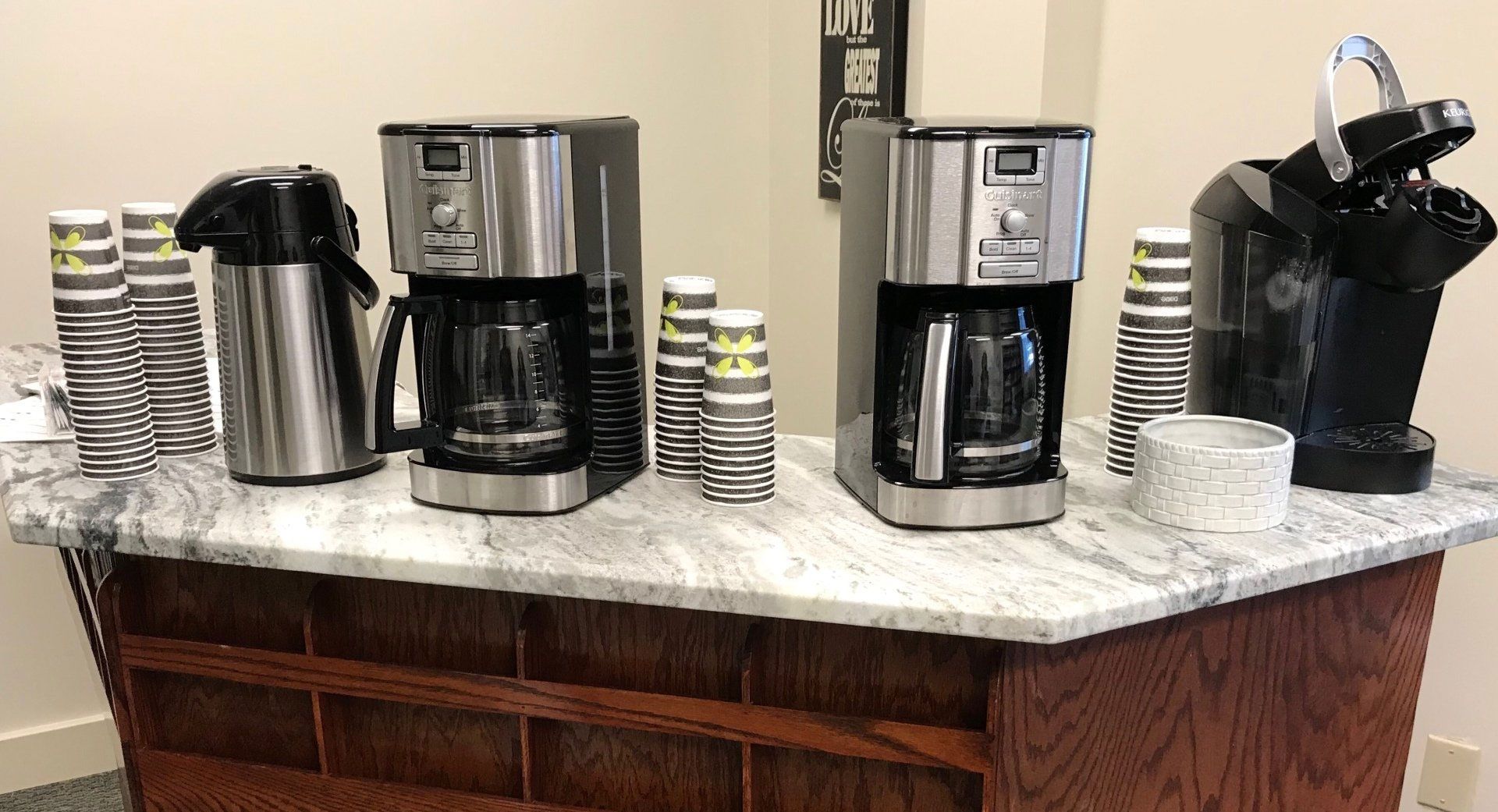 A counter with coffee makers , thermoses , and cups on it.