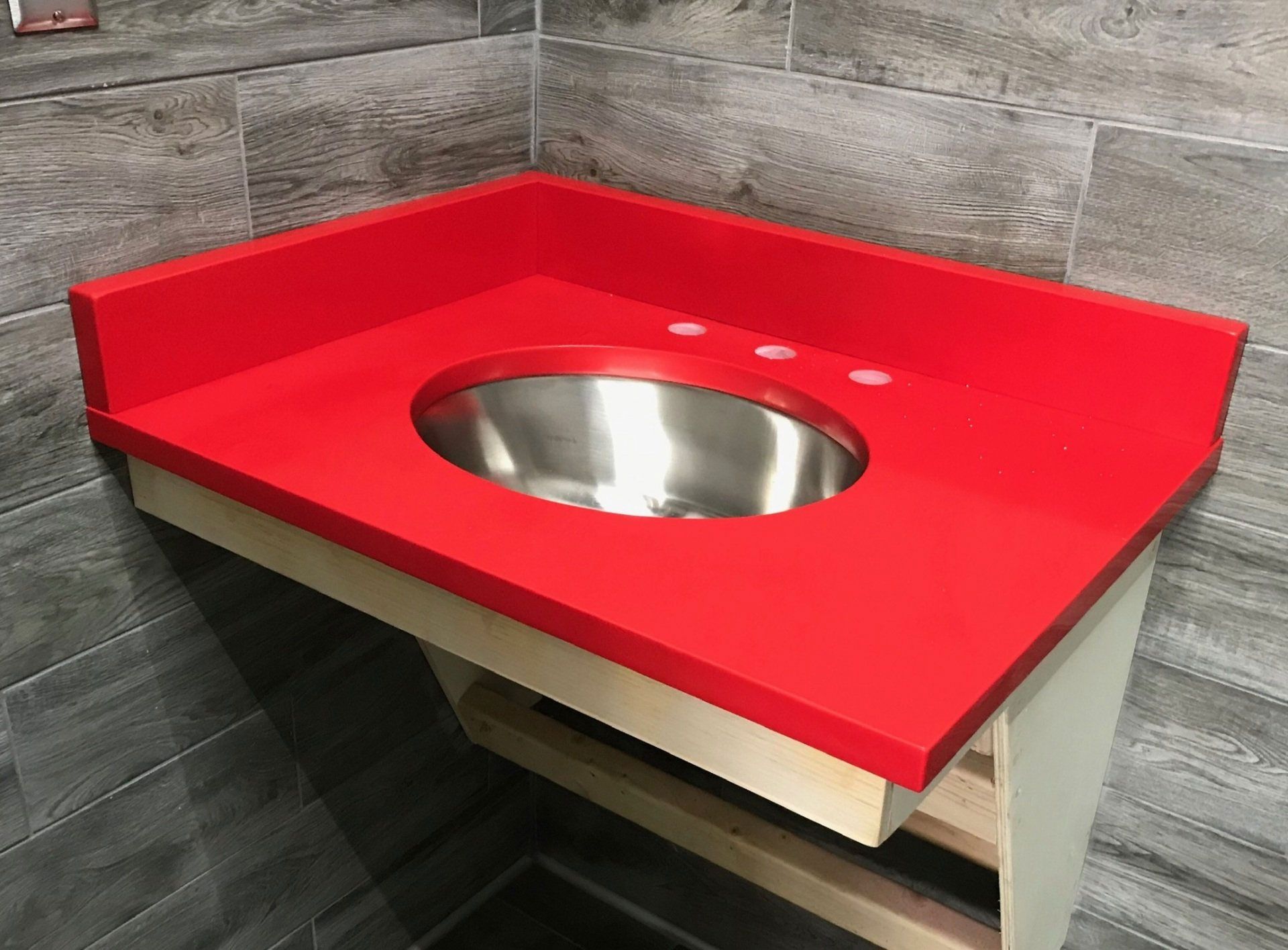 A bathroom sink with a red counter top and a stainless steel sink