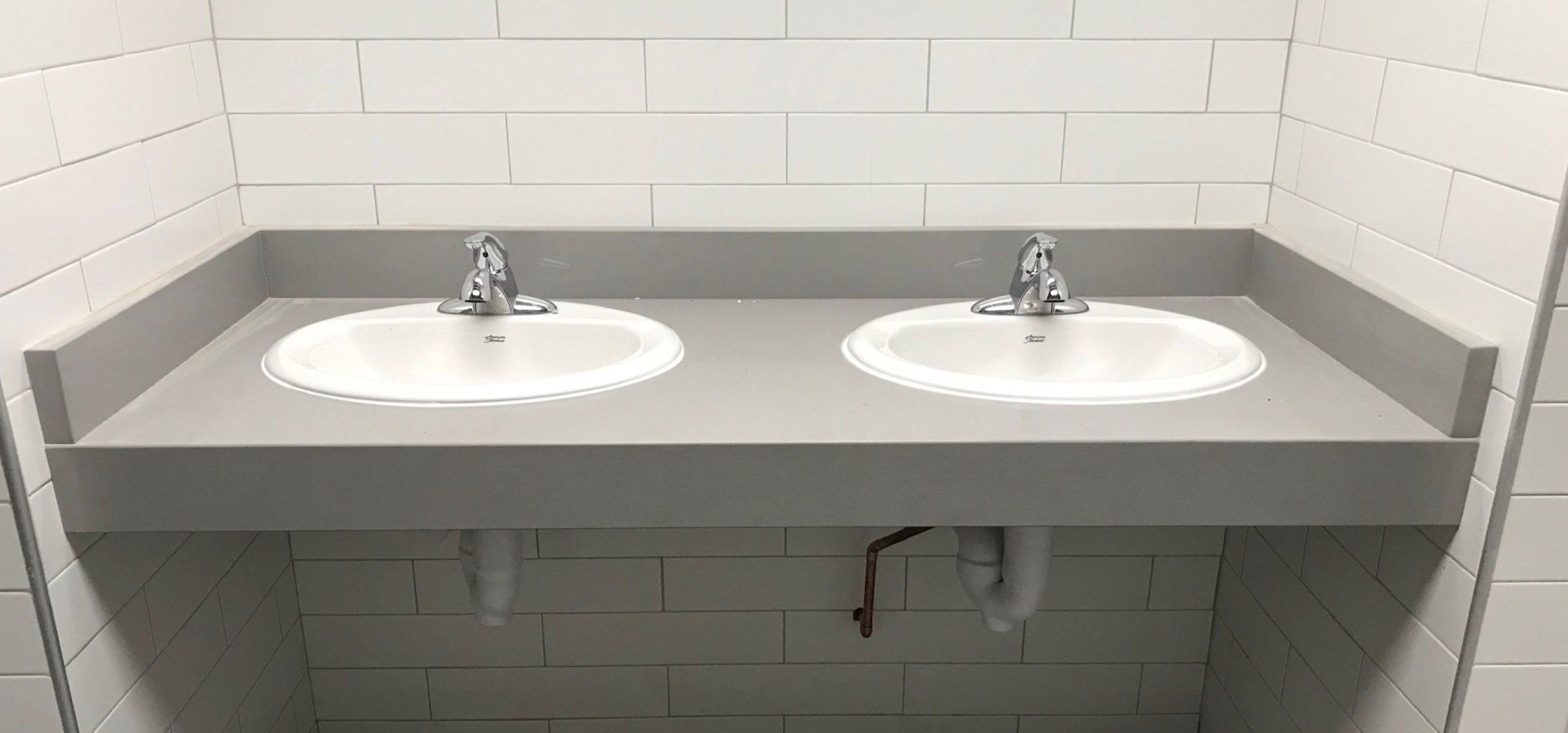 There are two sinks in a bathroom with white tiles.