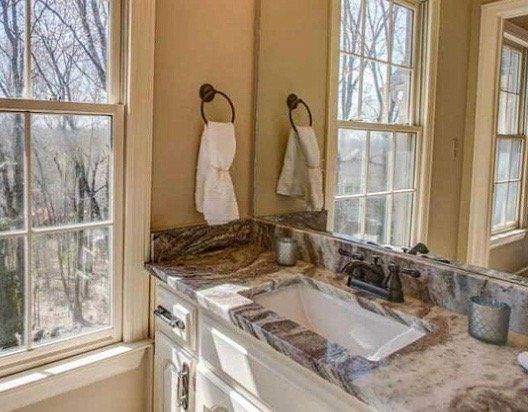 A bathroom with a sink , mirror and window.