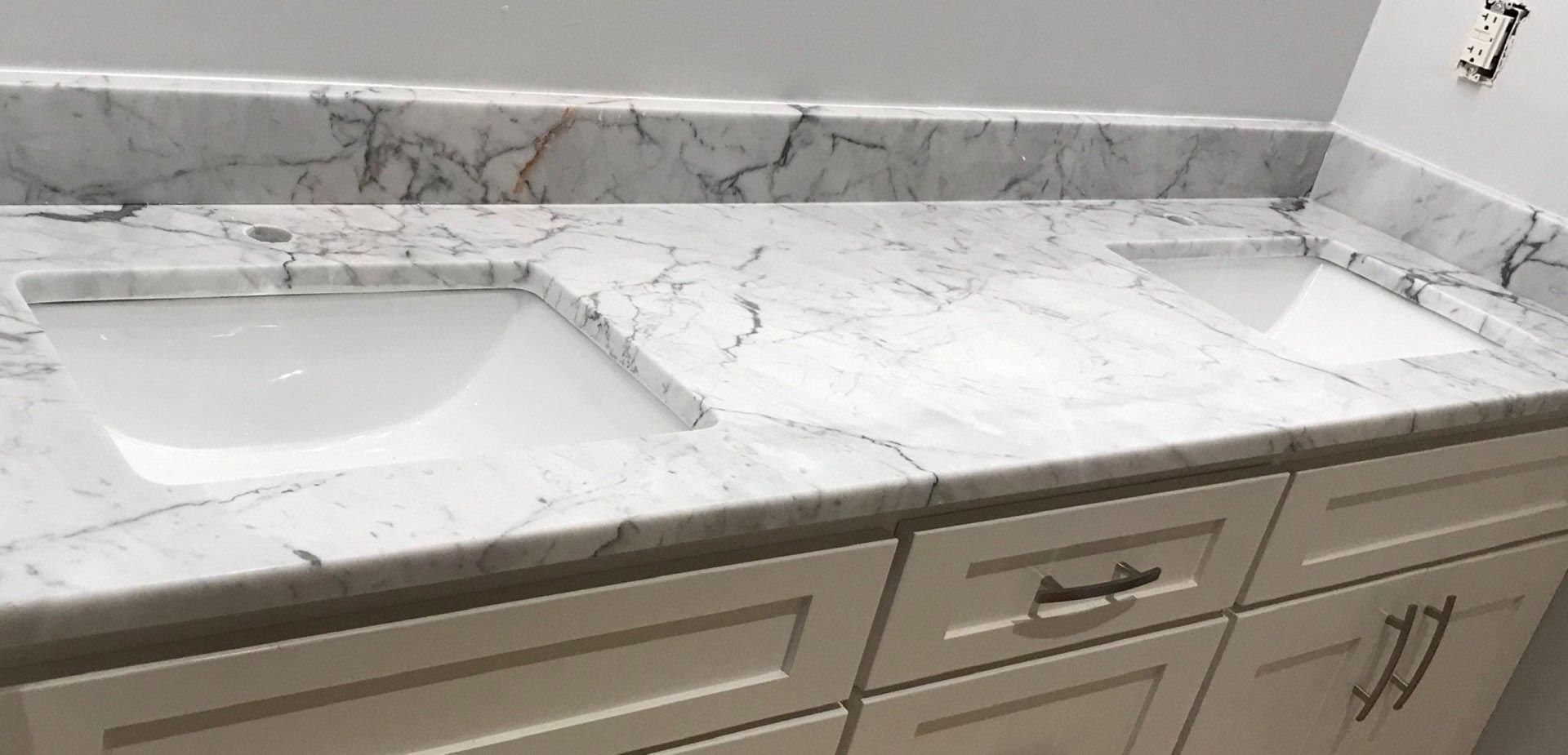 A bathroom sink with a marble counter top and white cabinets.