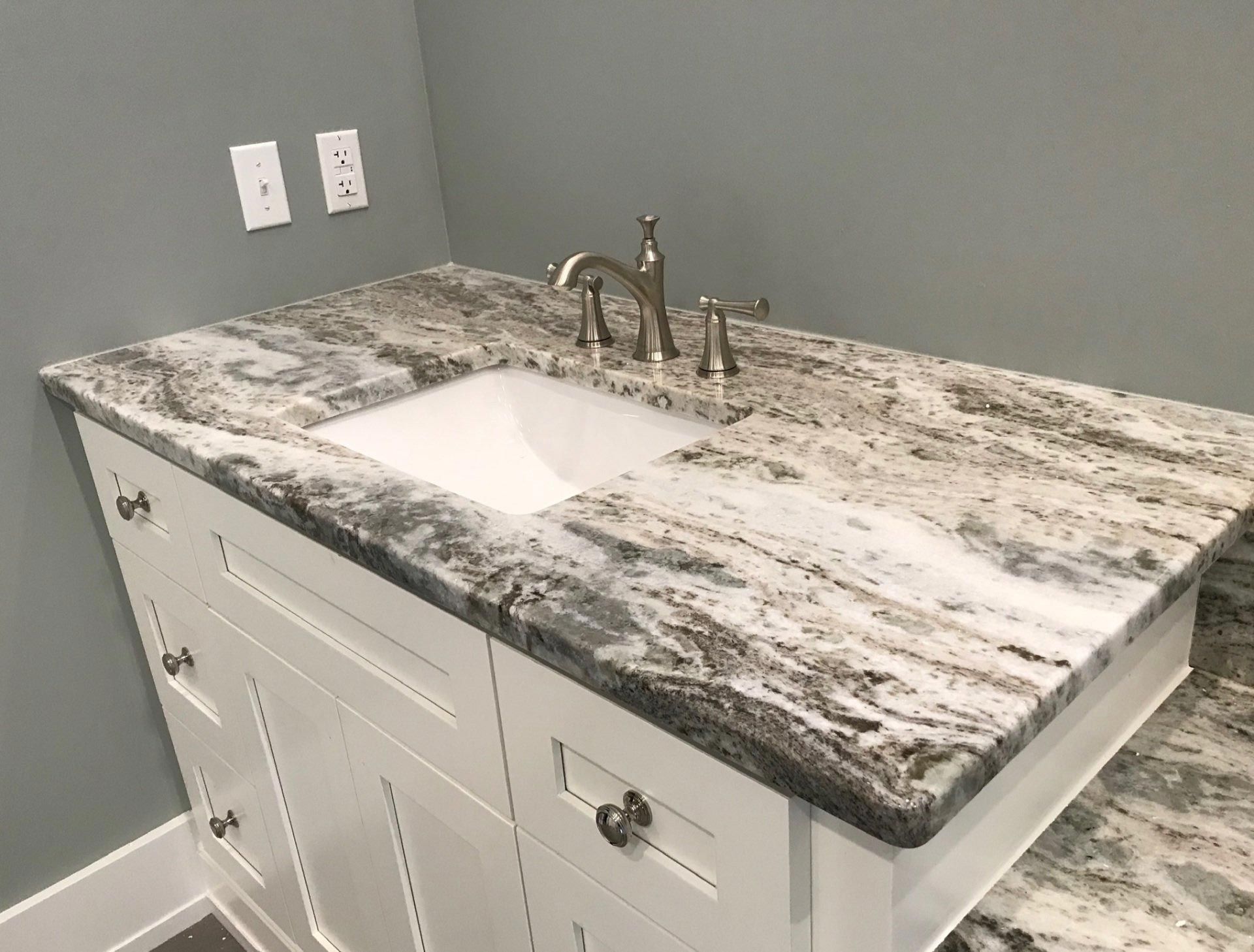 A bathroom vanity with a granite counter top and a sink.