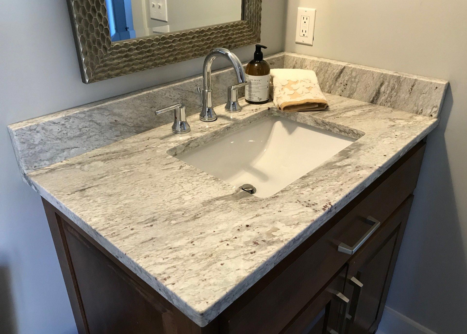 A bathroom sink with a granite counter top and a mirror.