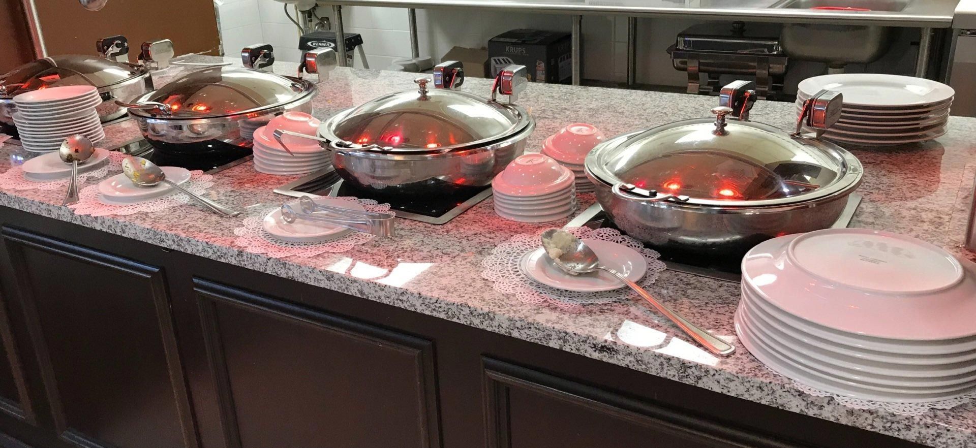 A buffet table with plates , pots and pans on it.