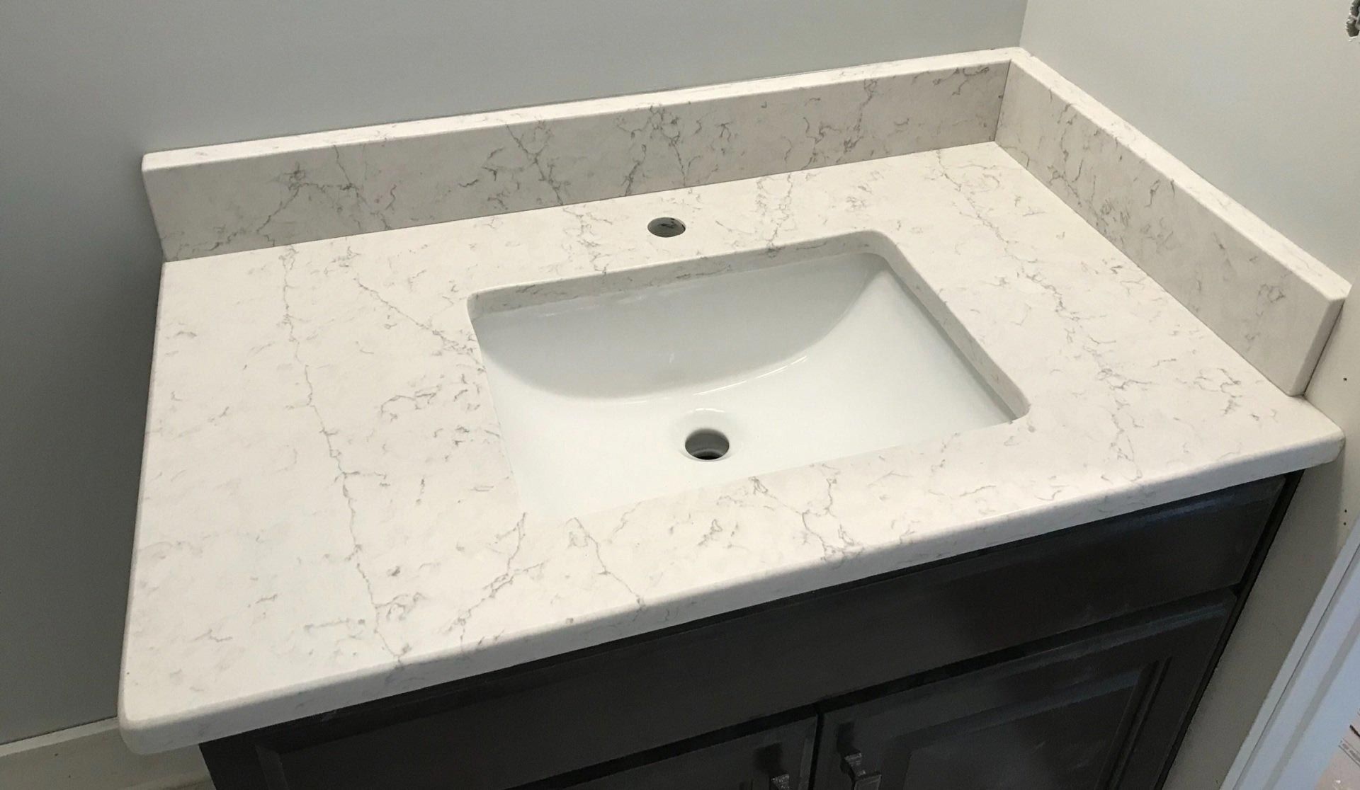 A bathroom sink with a white counter top and a black cabinet.