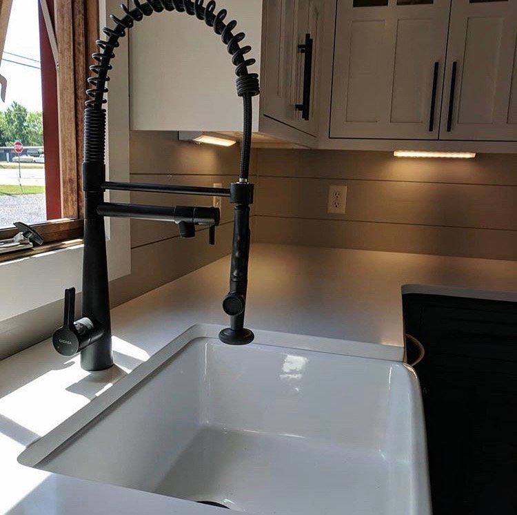 A kitchen sink with a black faucet and a window