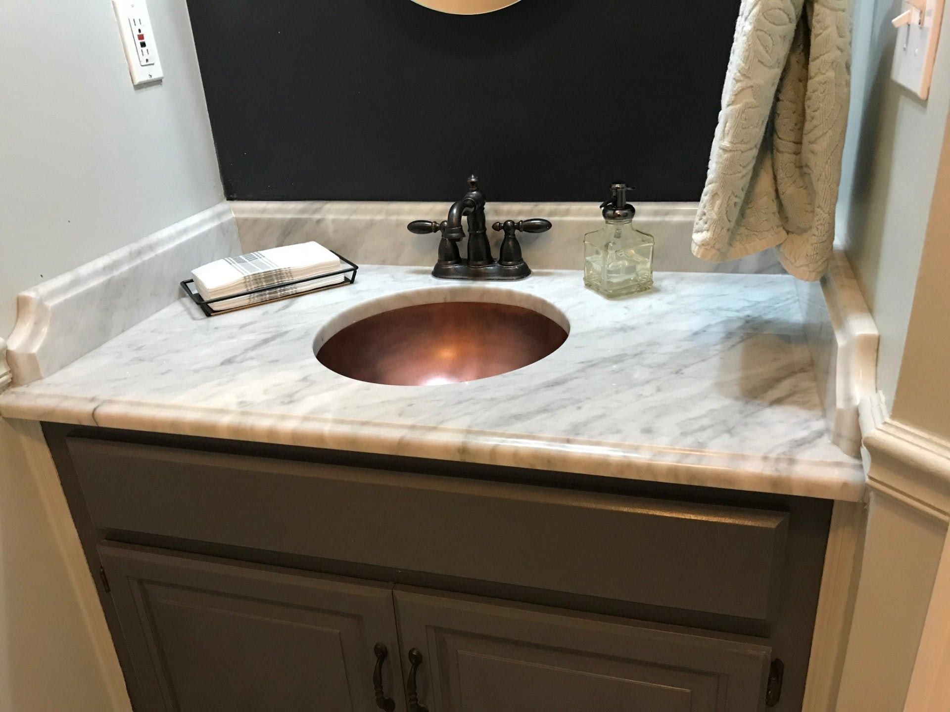 A bathroom sink with a marble counter top and a copper sink.