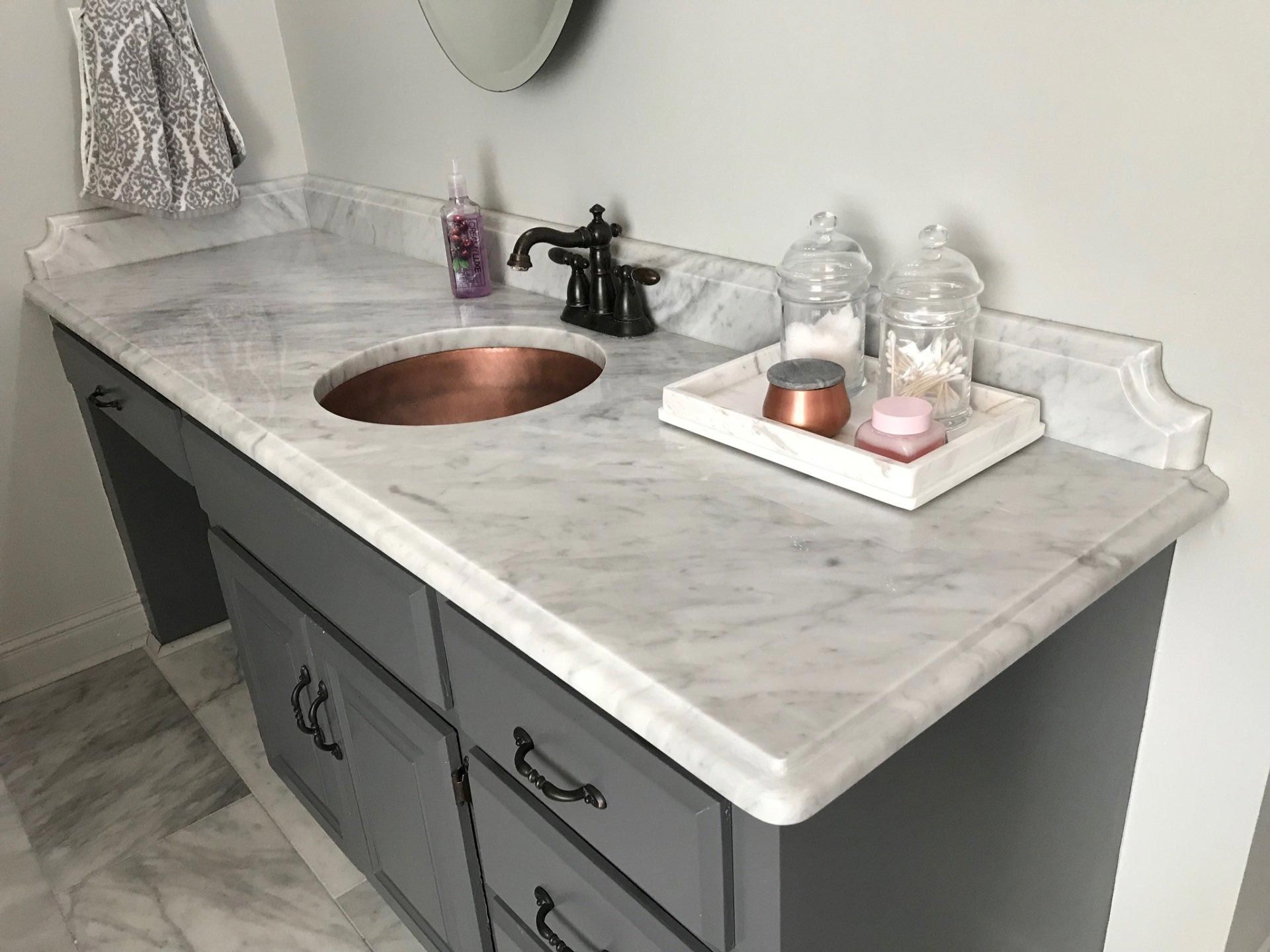 A bathroom vanity with a marble counter top and a copper sink.