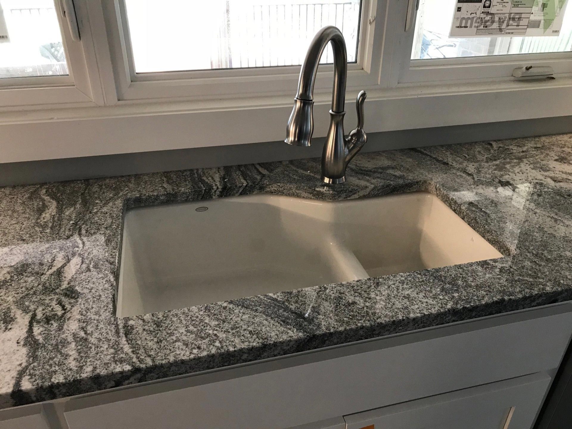 A kitchen sink with a faucet on a granite counter top.