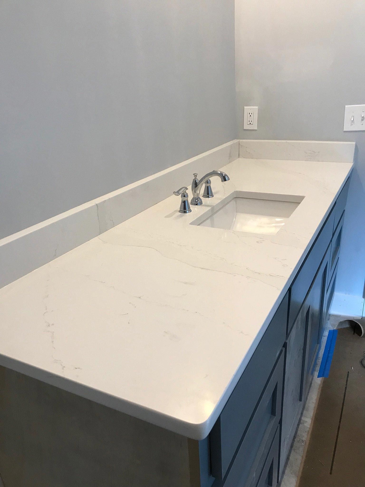 A bathroom sink with a white counter top and blue cabinets.