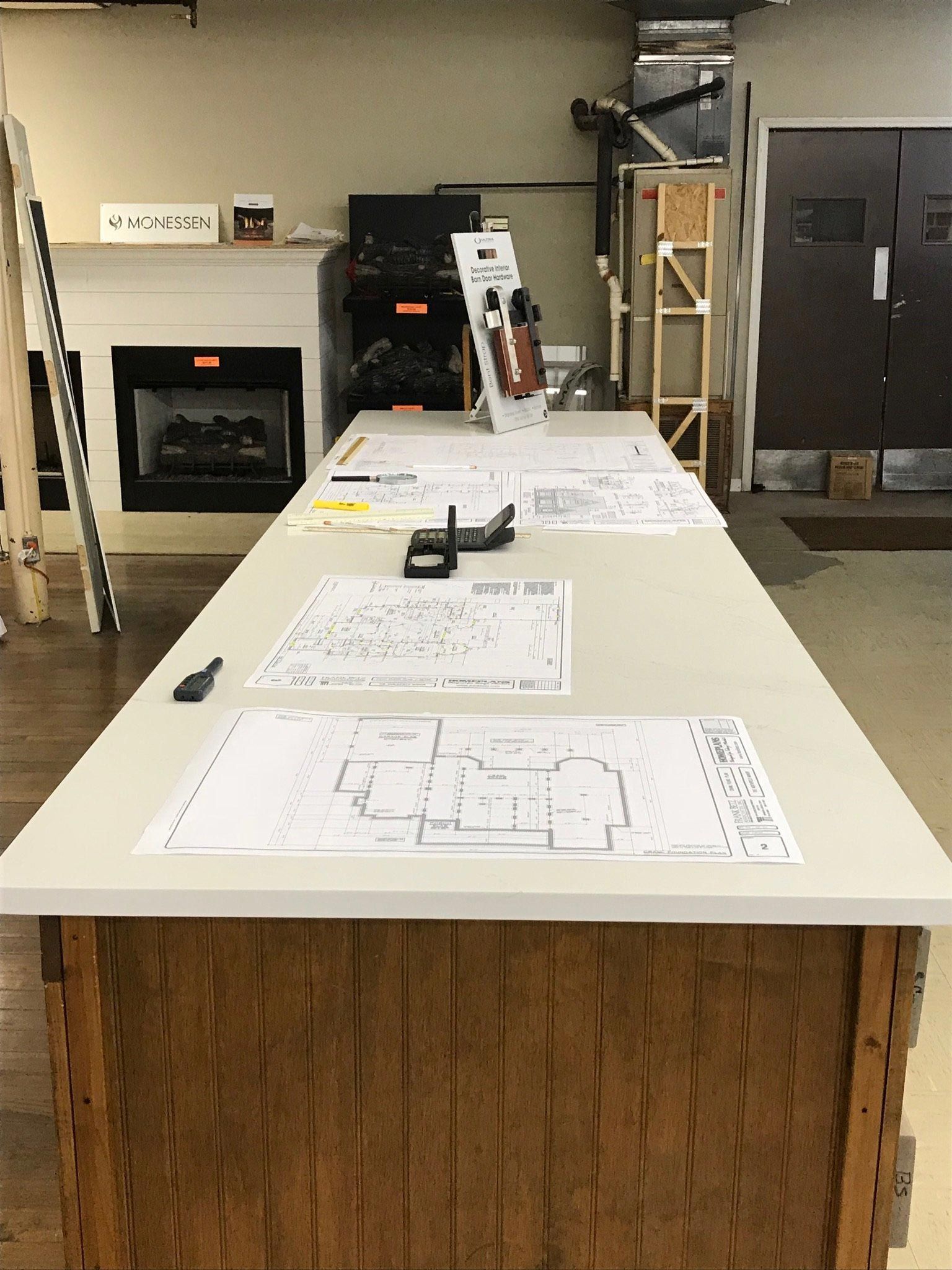 A long table with drawings on it in a room with a fireplace