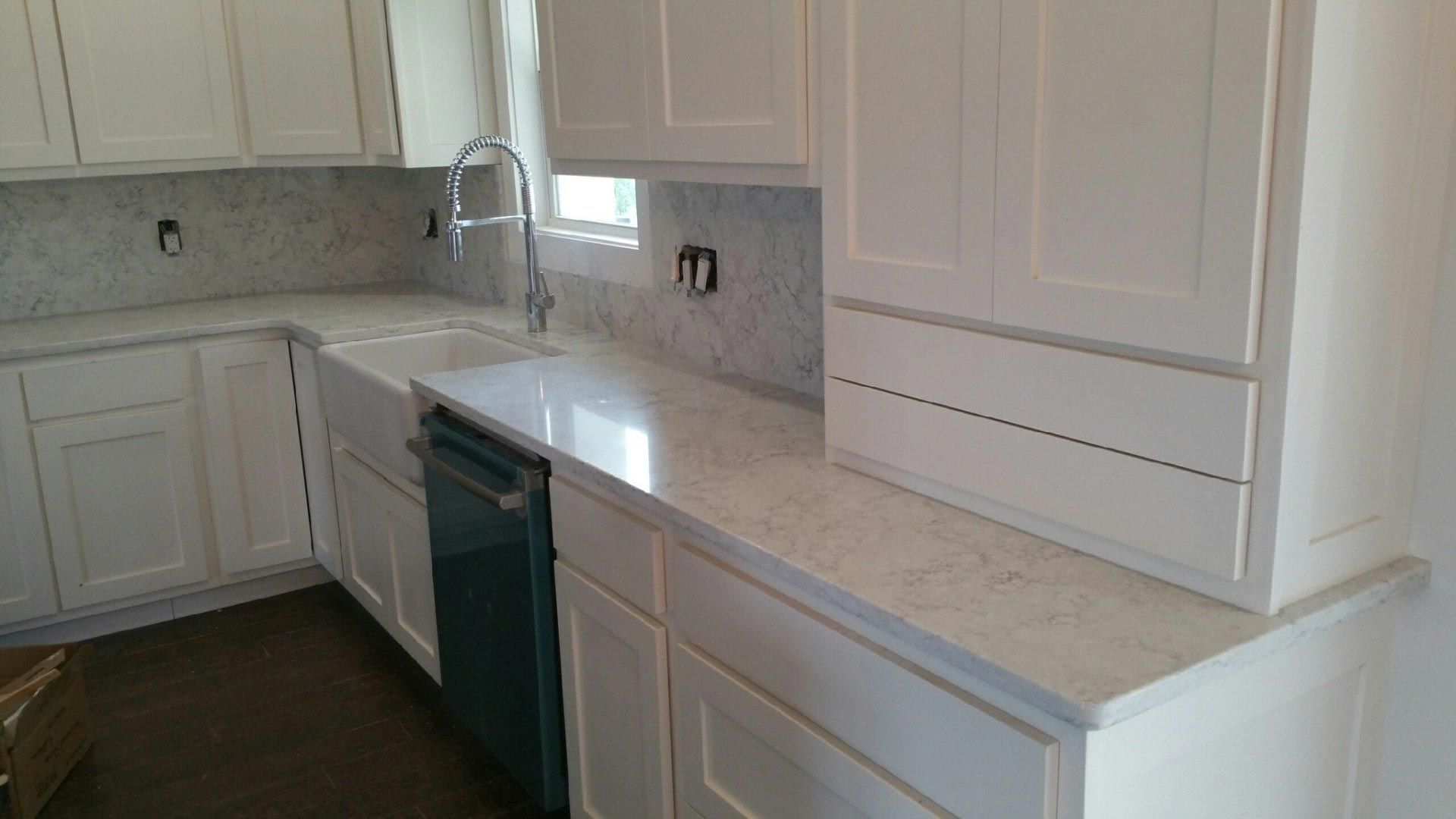 A kitchen with white cabinets , white counter tops , and a black dishwasher.