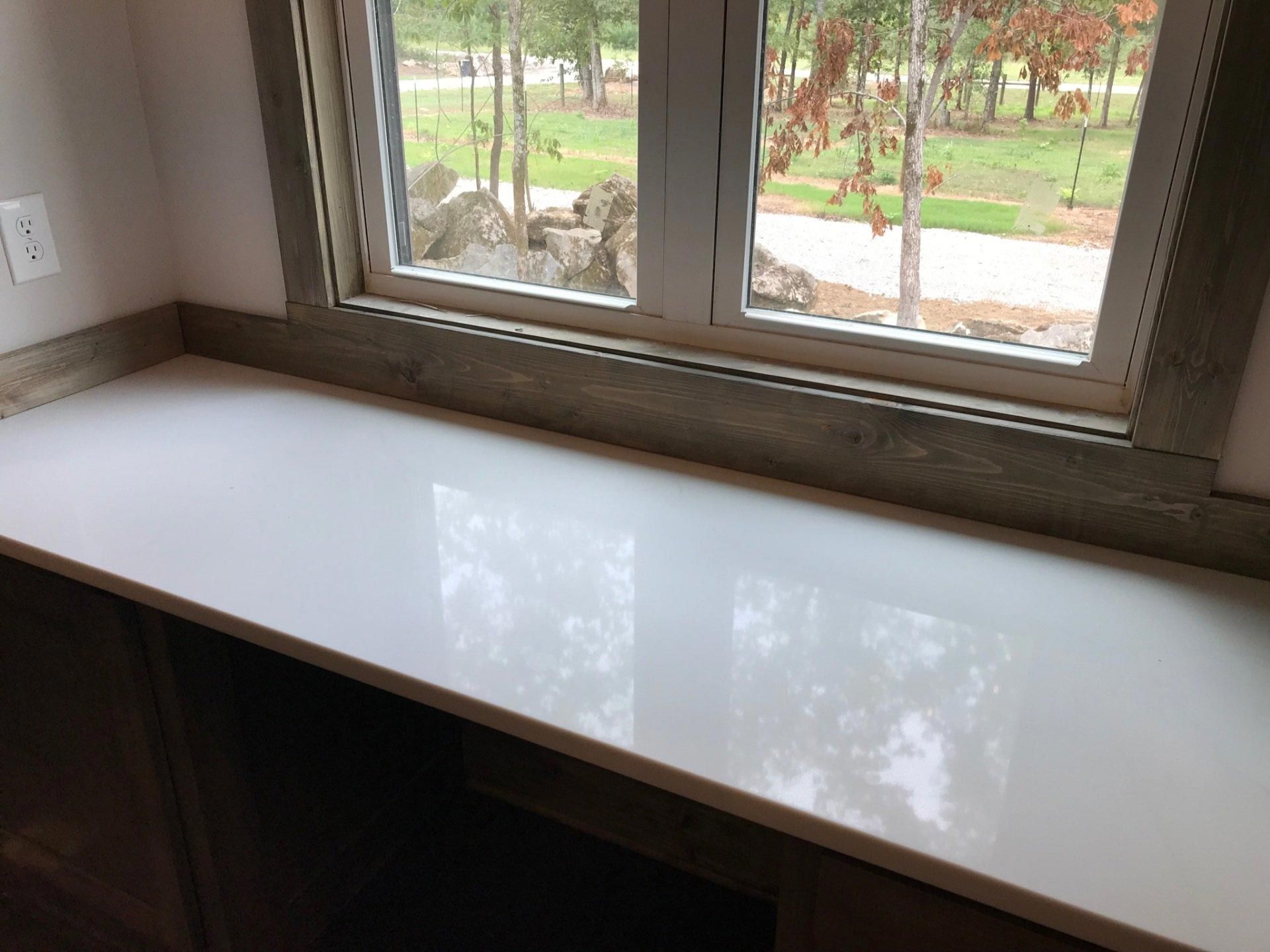 A white counter top next to a window with a view of a park.