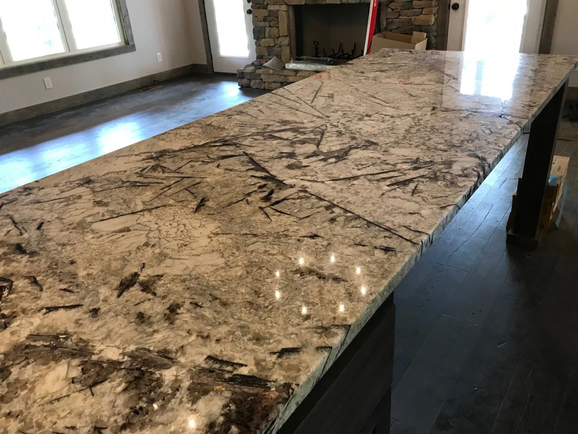 A large granite counter top in a kitchen with a fireplace in the background.