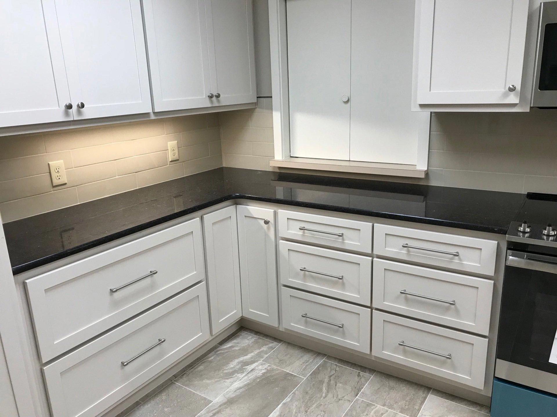 A kitchen with white cabinets and black counter tops.