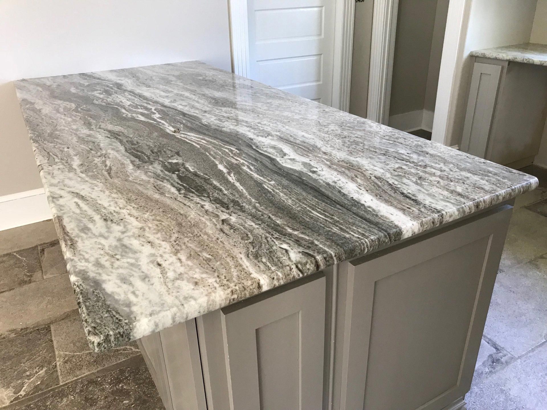 A kitchen island with a granite counter top and gray cabinets.