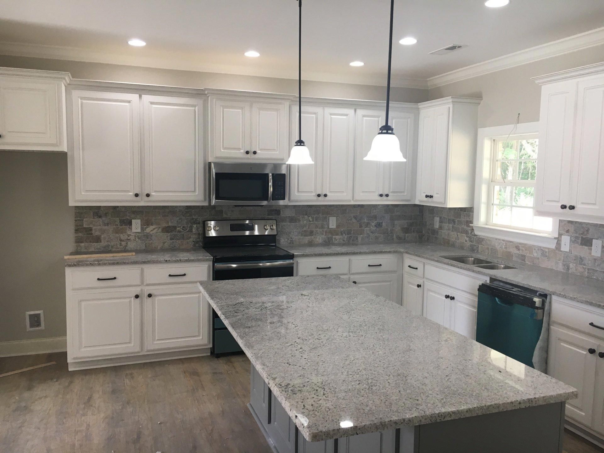 A kitchen with white cabinets , granite counter tops , stainless steel appliances and a large island.