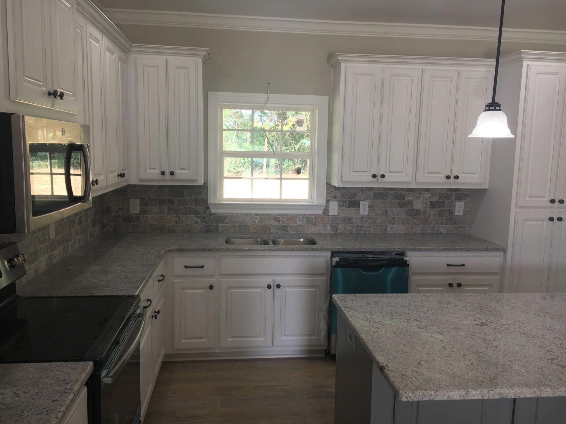 A kitchen with white cabinets , granite counter tops , stainless steel appliances and a window.