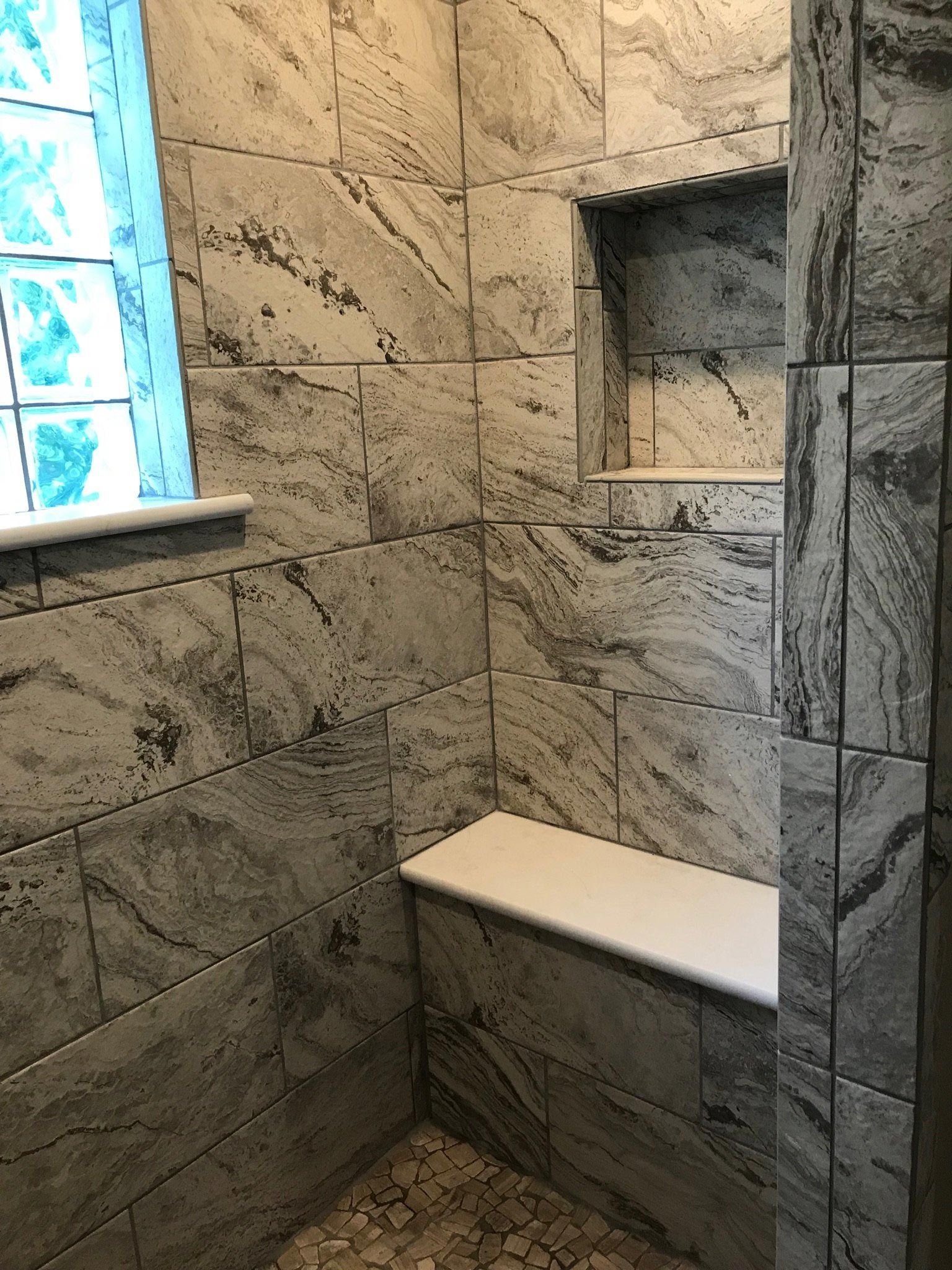 A shower with a bench and a window in it.