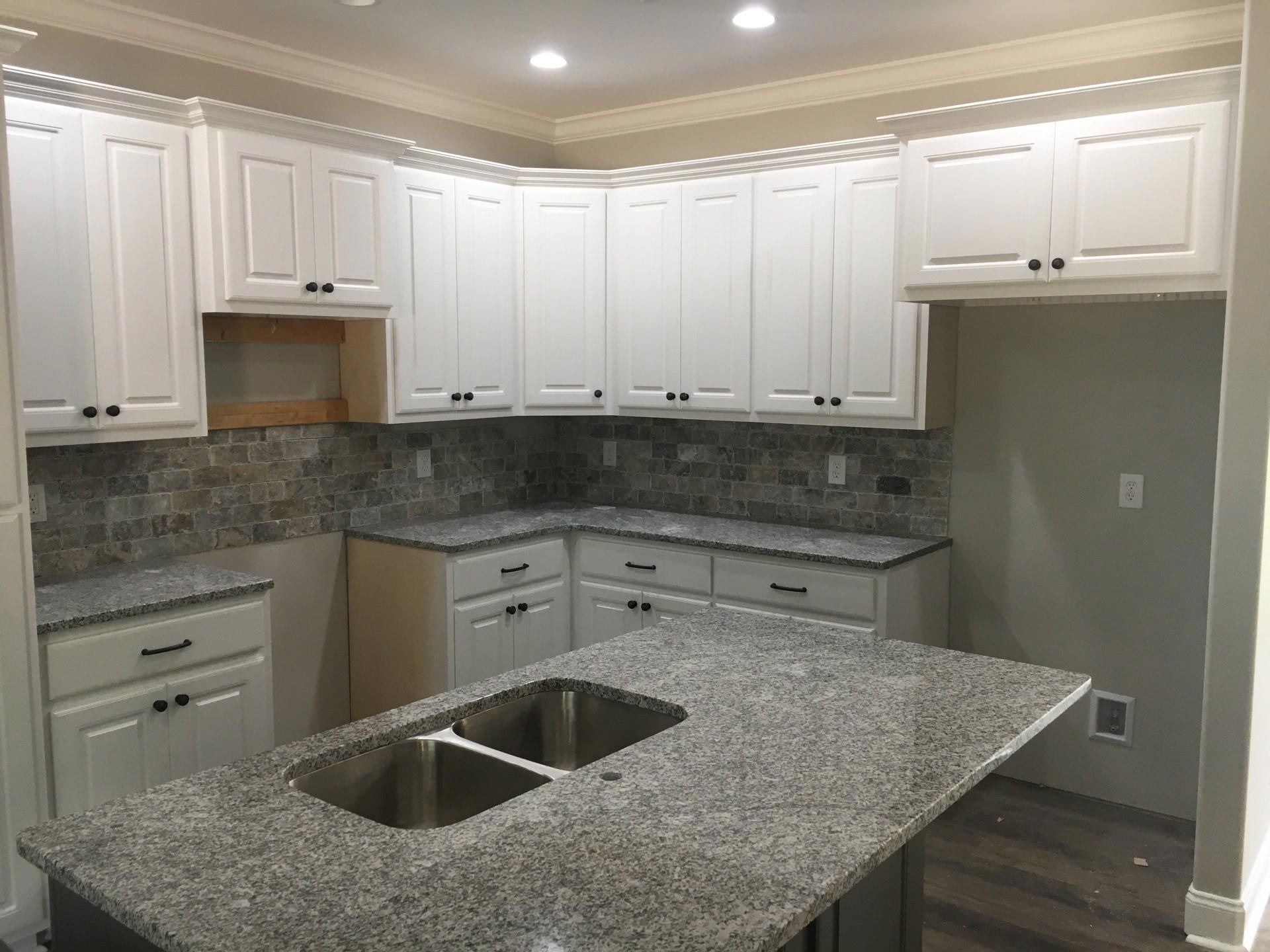 A kitchen with white cabinets , granite counter tops , and a sink.