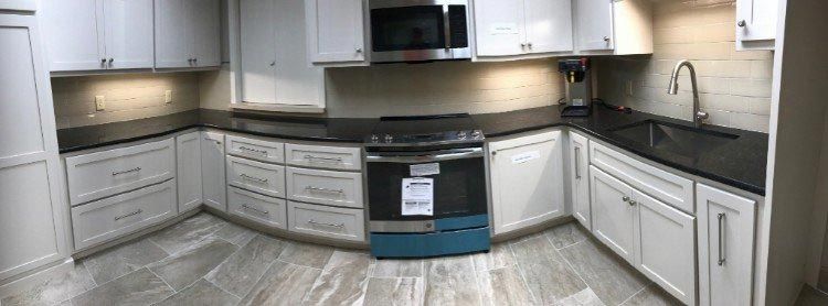 A kitchen with white cabinets , black counter tops , stainless steel appliances , and a sink.