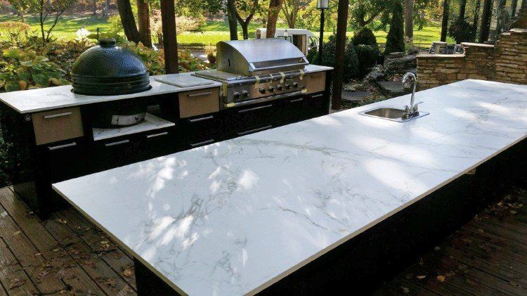 A large outdoor kitchen with a marble counter top and a grill.