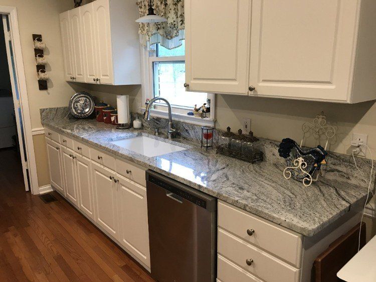 A kitchen with white cabinets , granite counter tops , a sink and a dishwasher.