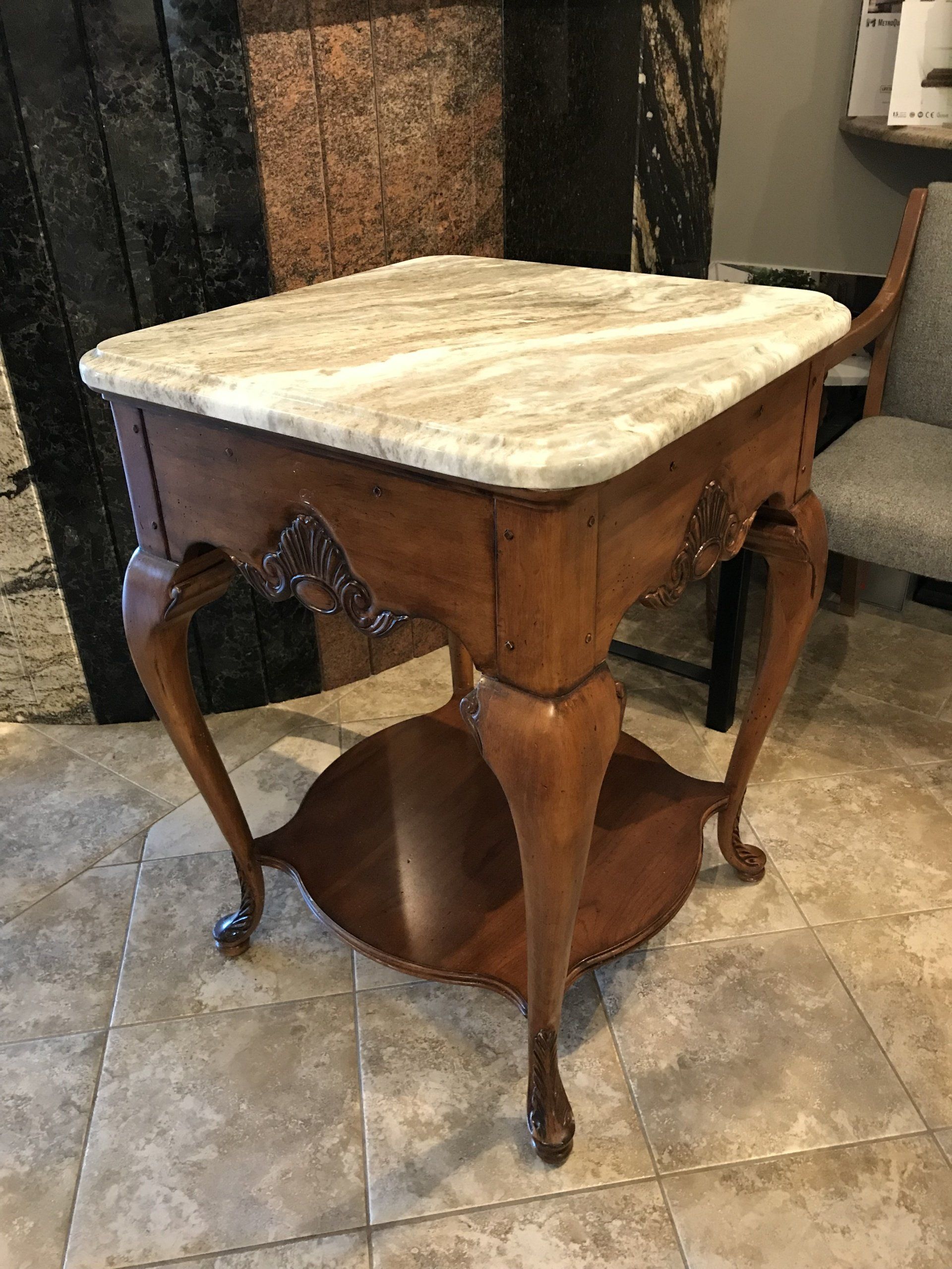 A small wooden table with a marble top is sitting on a tiled floor.