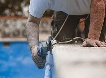 Person using a grinder to work on the edge of a swimming pool.