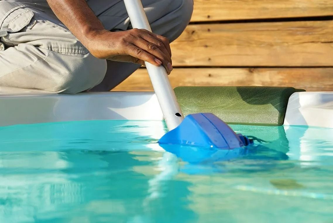 Person cleaning a pool with a blue vacuum head attached to a pole.