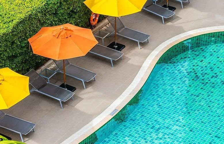 Poolside scene with orange and yellow umbrellas, lounge chairs, and turquoise water.