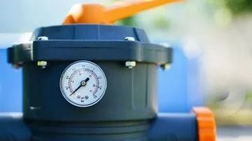 Black water filter with orange handle and pressure gauge.