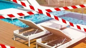 Pool area closed with red and white caution tape. Two empty lounge chairs next to the water.