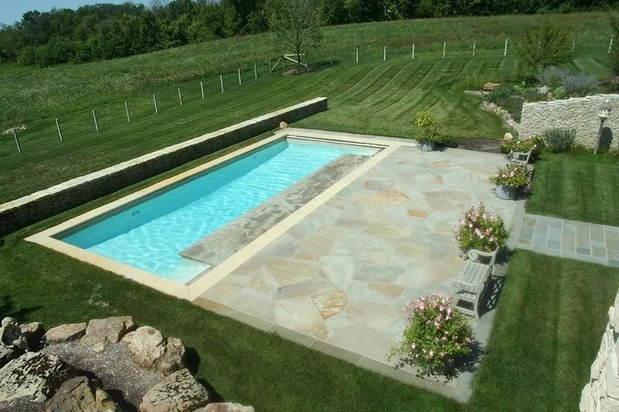 Rectangular pool with light blue water, surrounded by patio, lawn, and greenery.