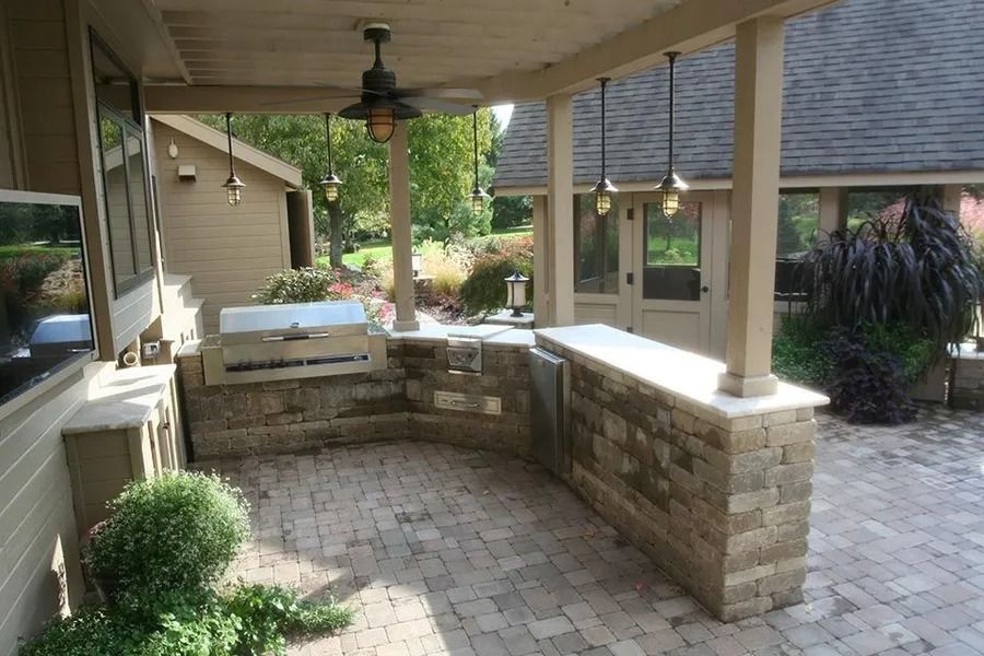 Outdoor kitchen with brick patio, built-in grill, and hanging lights under a covered patio with a fan.