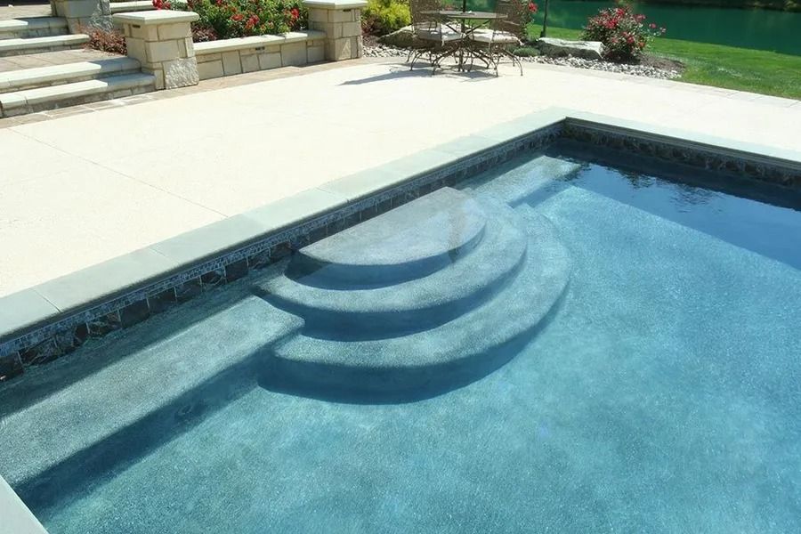 Pool with curved steps, blue water, and stone surround.