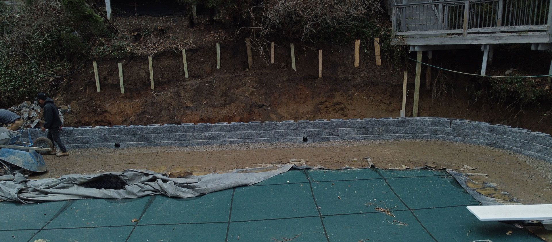 A person near a pool covered by a green tarp. There's a deck and a hillside in the background.