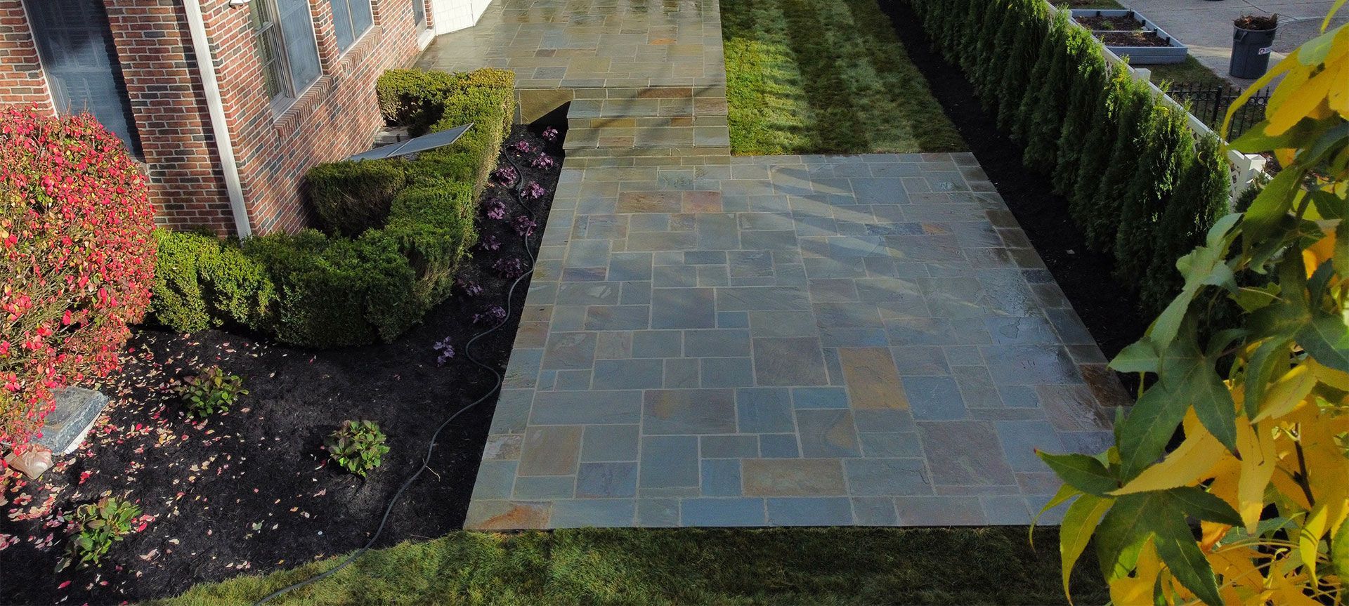 Stone patio with manicured landscaping next to a brick building.