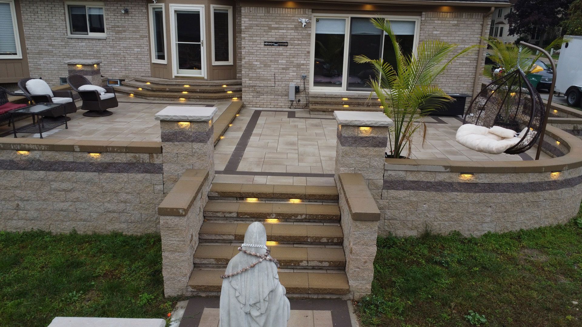 Stone steps and patio lead to a house with built-in lighting. A statue stands on the lower steps.
