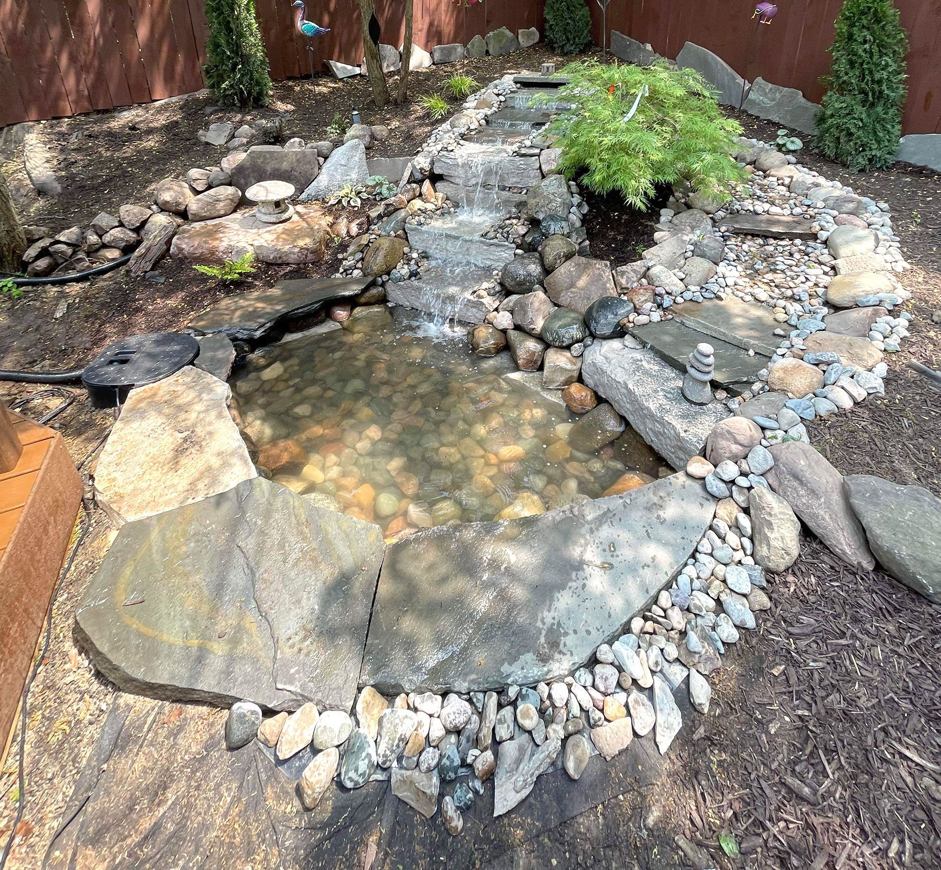 A small backyard pond with a waterfall, surrounded by rocks and greenery.