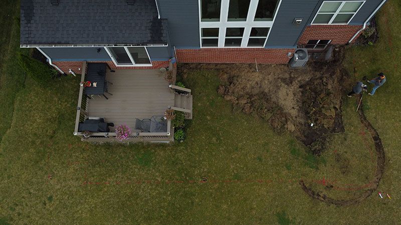 Backyard with house and deck; person on lawn, and exposed earth.