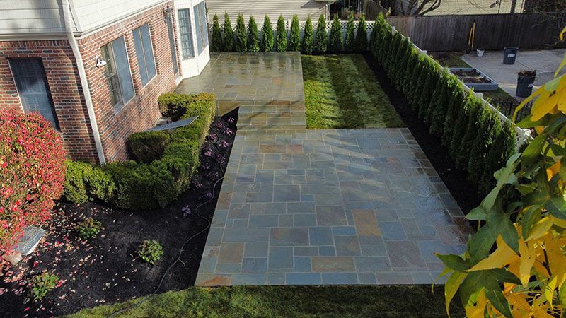 Brick house with a stone patio, manicured hedges, and a narrow grass strip.