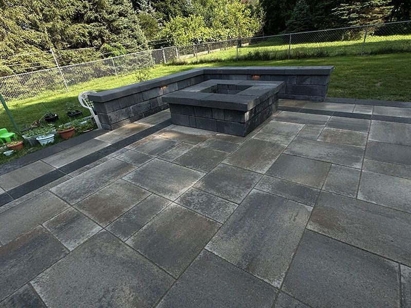 Patio with dark gray pavers, fire pit, and retaining wall. Green lawn in the background.