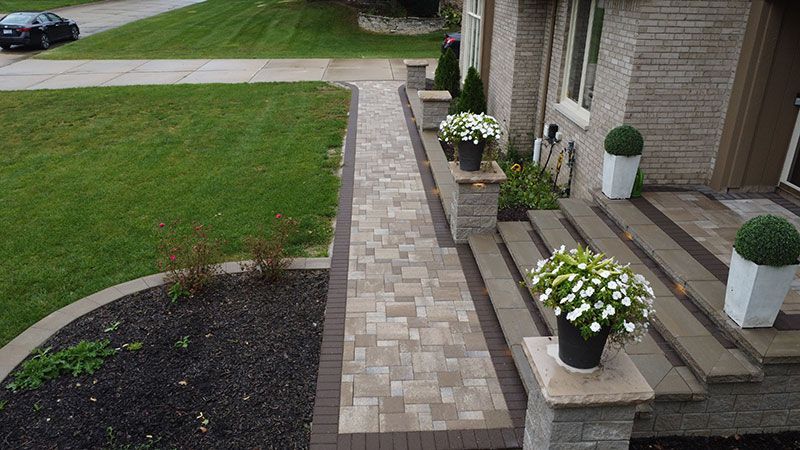 A brick pathway leading to a house with steps and potted flowers.