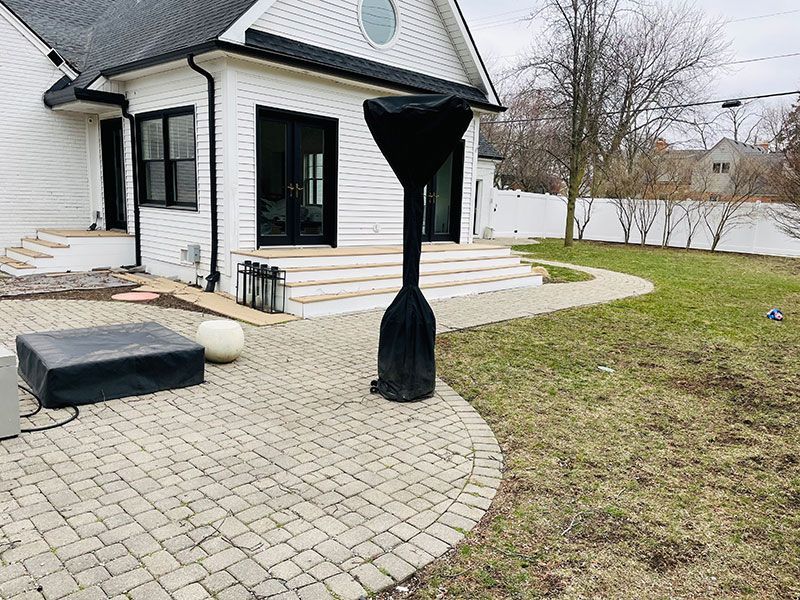 Backyard patio with covered heater, home's white exterior, stone pathway, and green lawn.