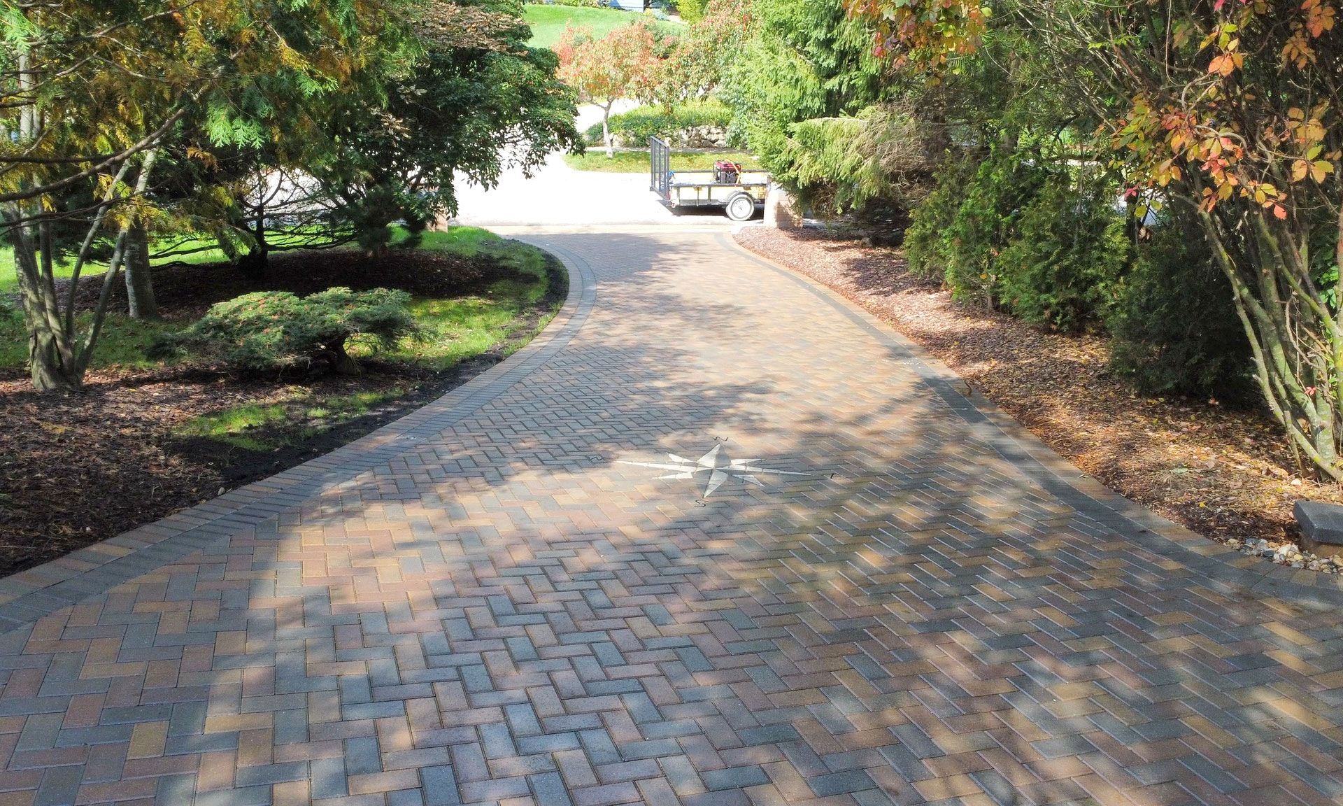 Brick driveway curves towards a distant house, flanked by trees with autumn foliage.