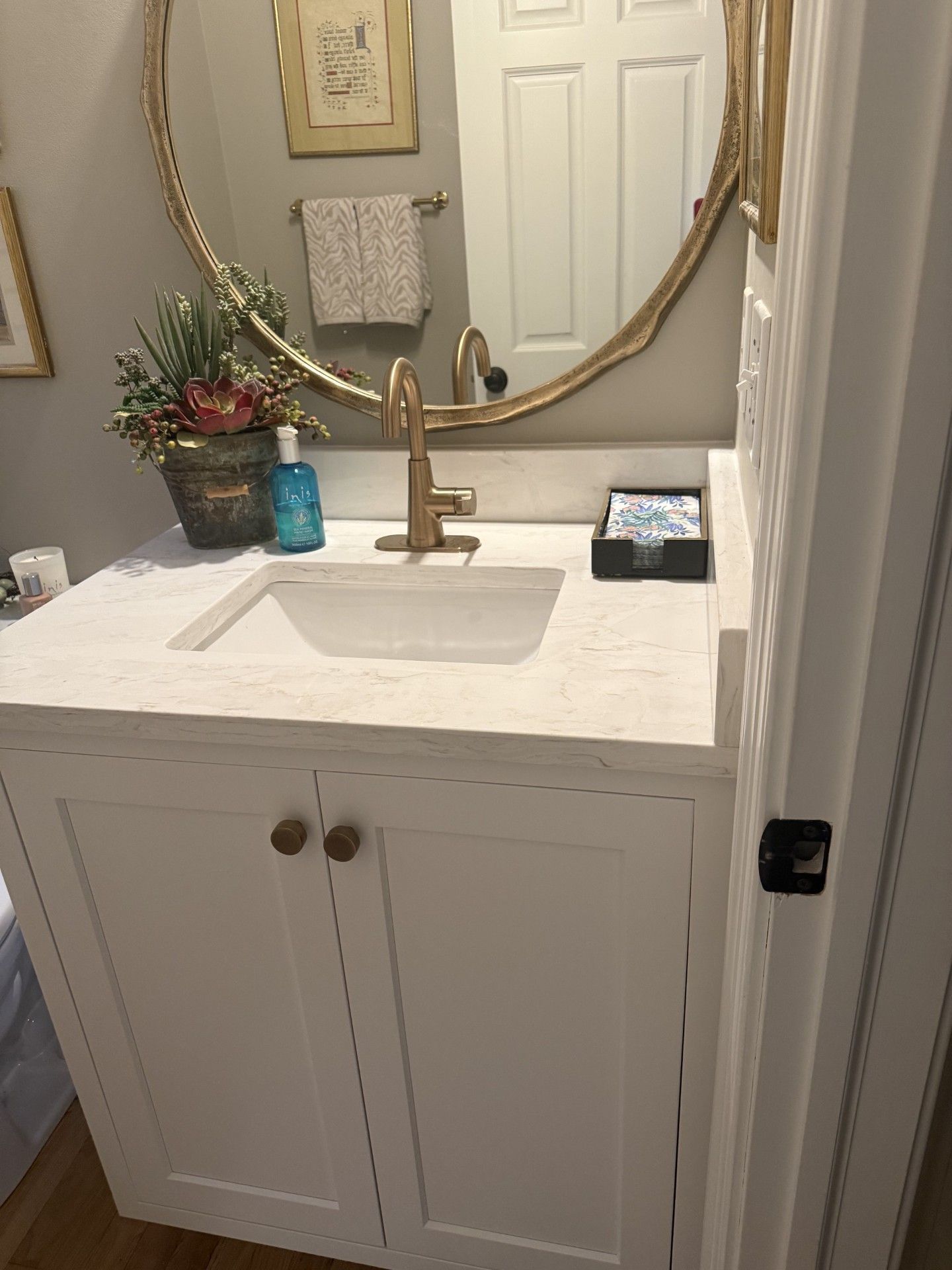 Bathroom vanity with white cabinet, sink, round mirror, and small plant by a towel rack