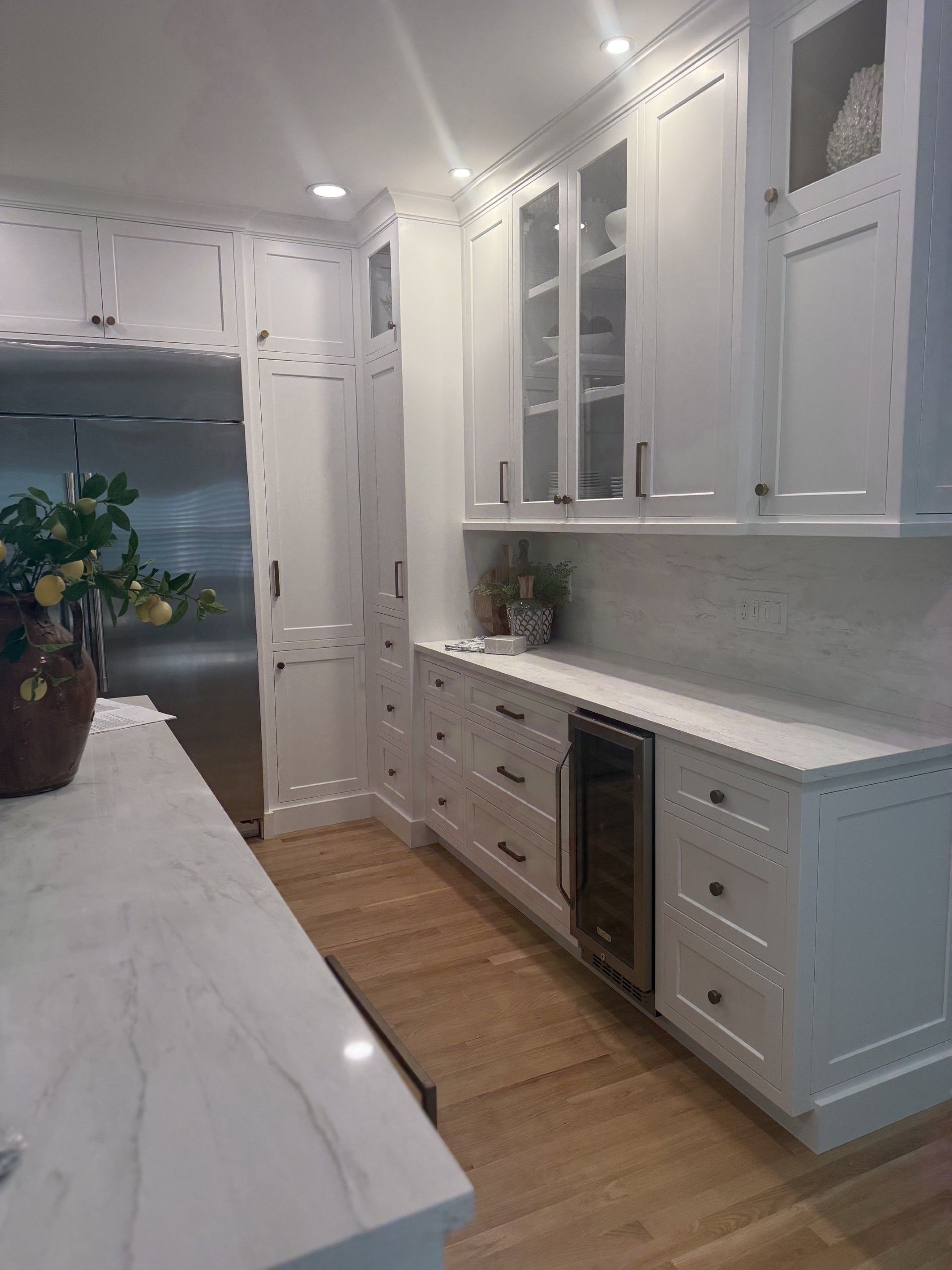 Bright white galley kitchen with marble counters, glass cabinets, and wood floors