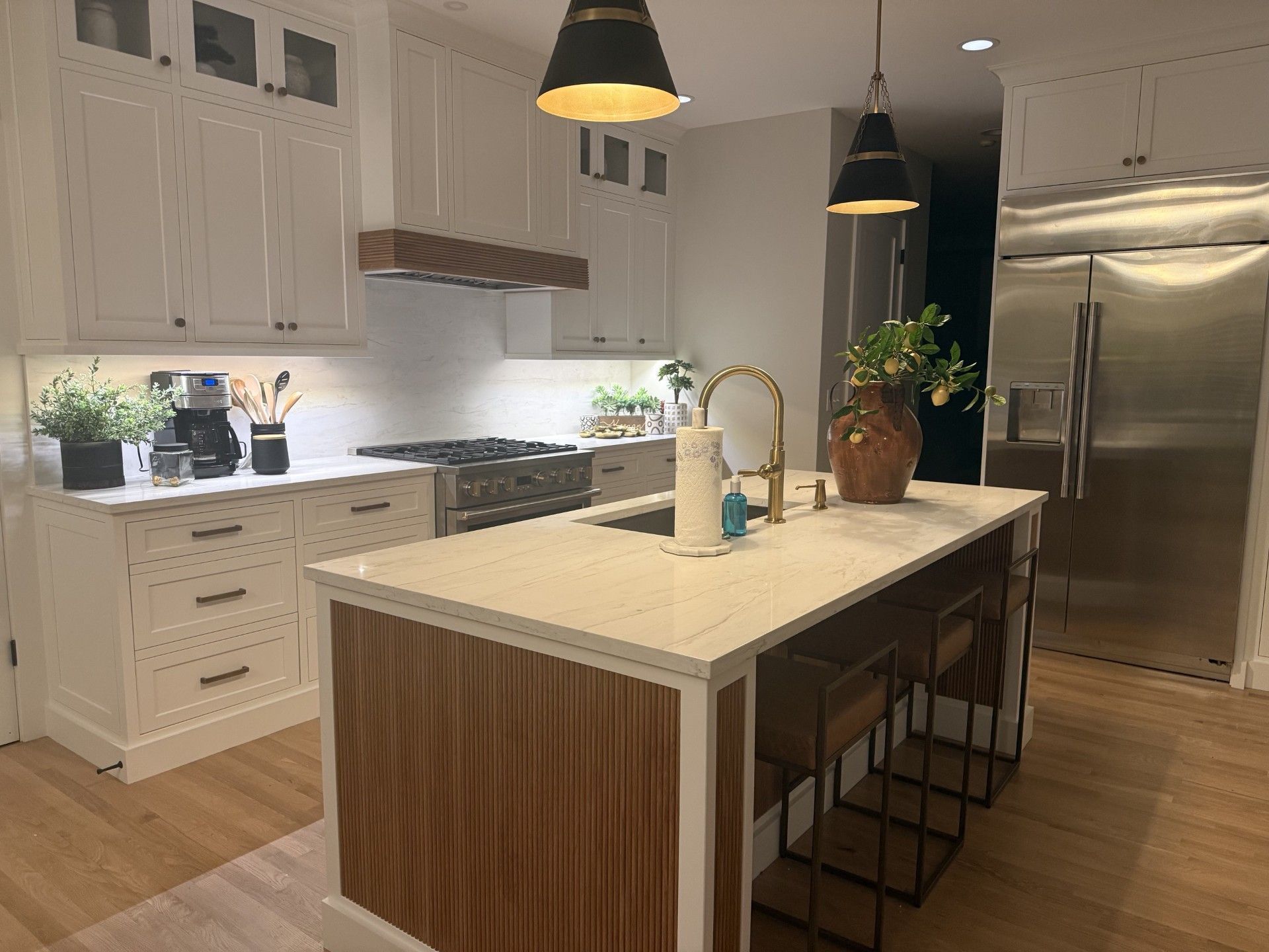 Modern white kitchen with a large island, black pendant lights, and stainless steel refrigerator